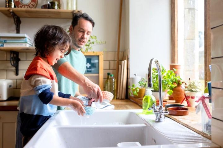 Father and son washing dishes in kitchen sink
