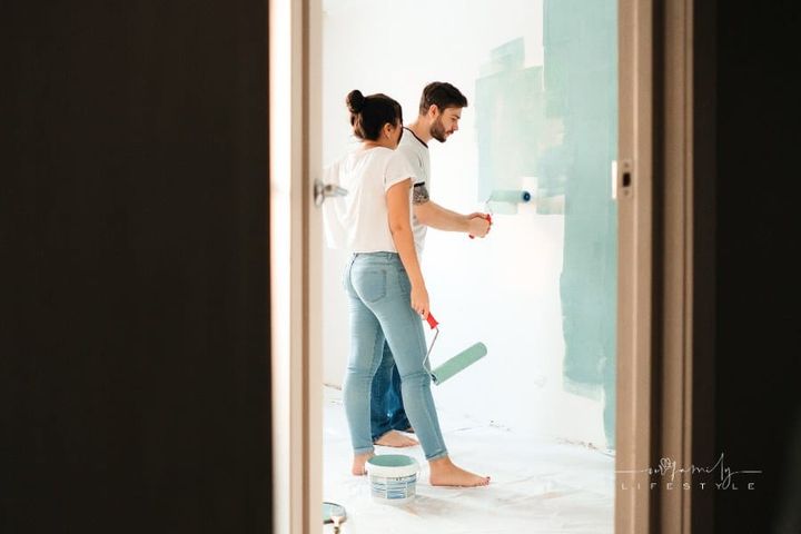 Man Painting Wall Beside a Woman holding a Paint Roller