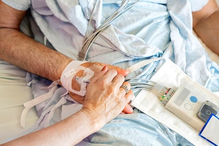 wife holding husband's hand as he lays in a hospital bed