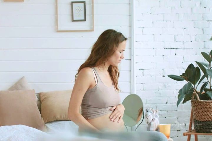 Closeup expectant mother suffering nausea in bedroom. Pregnant trying tea to help morning sickness.
