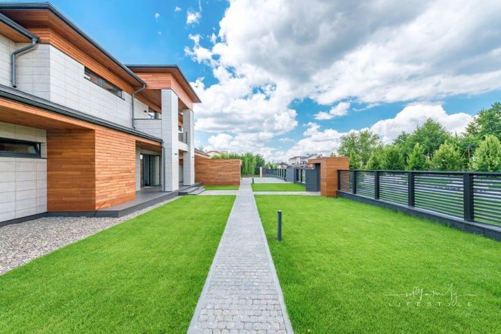 Yard of contemporary house with artificial grass and trees outside fence