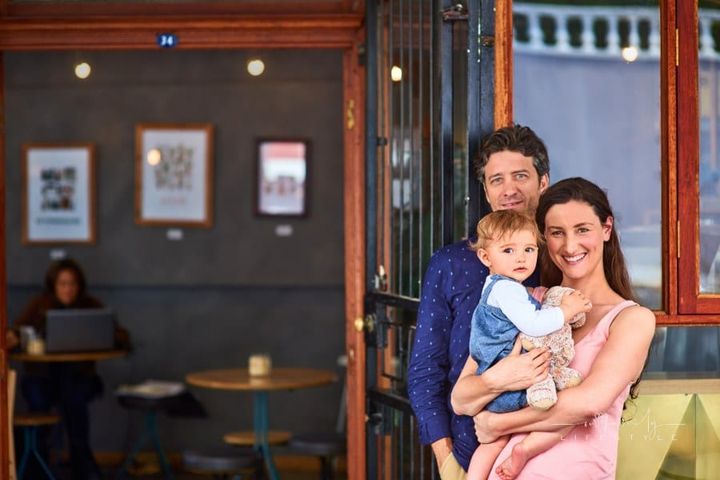 Portrait of smiling couple and their little girl standing in front of their cafe