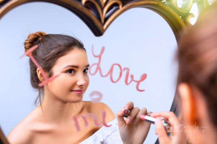 Portrait of a beautiful girl looking in the mirror and writing I love me near a heart, self-love