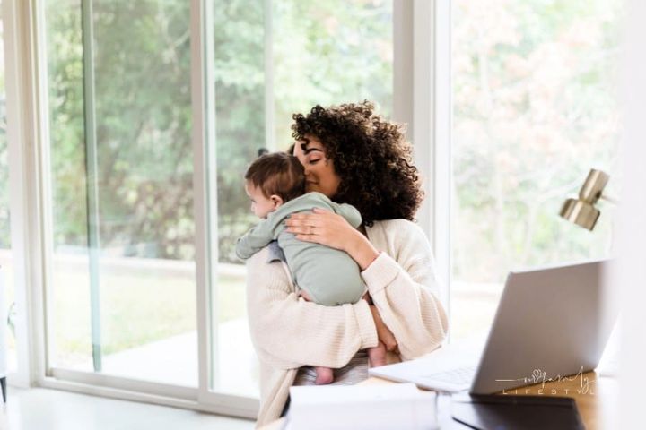 Mom multi-tasks on laptop while caring for newborn baby