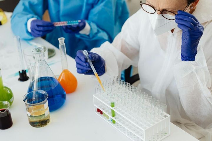 Scientists in protective gear working with liquids and test tubes in a lab.