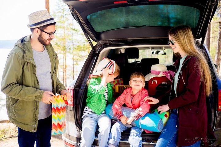 mother and father with two young daughters sitting in back of car while taking a break on a family road trip