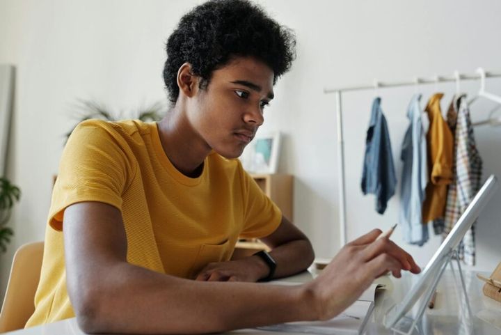 Teenage boy engaged in online learning using a tablet indoors.