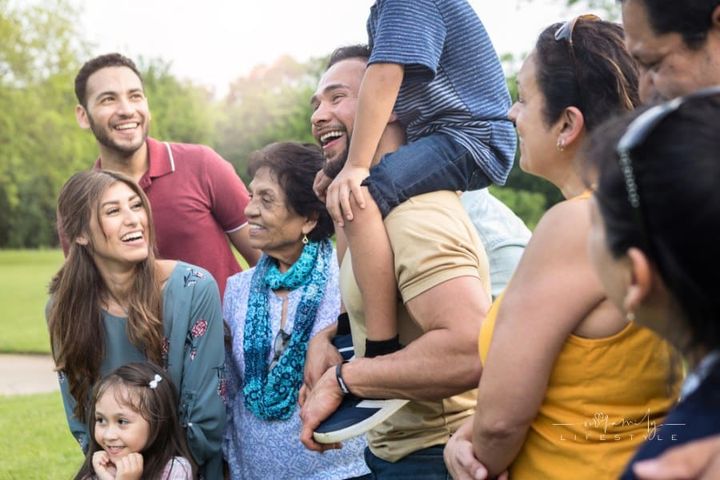 Large family enjoys picnic at the park on sunny day; preparing to take family photo