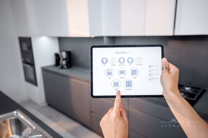Digital tablet with running mobile application to control smart devices in the kitchen. Female controlling smart devices remo
