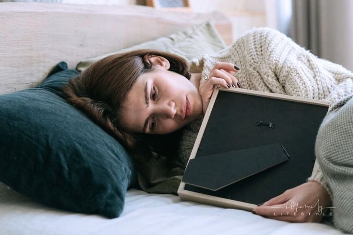 A Woman Lying on the Bed while Holding a Picture Frame