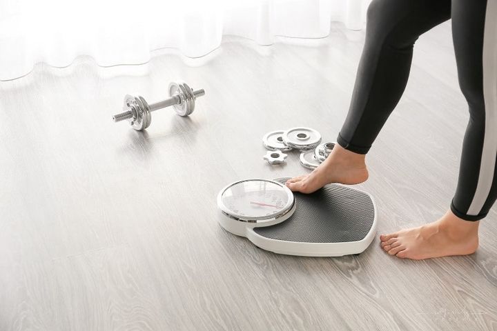 woman stepping on scale with weights and dumbbell nearby