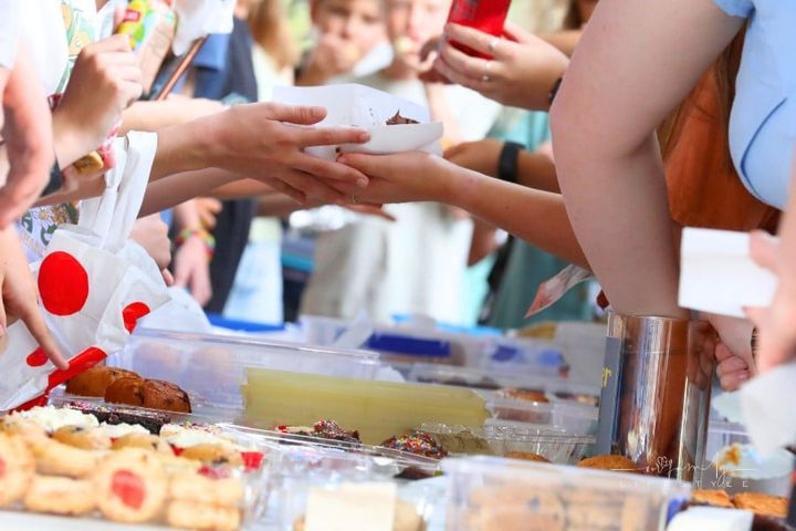 A close up of hands and food exchanging at a communty fair, fete or market stall. A typical bake or cake sale.