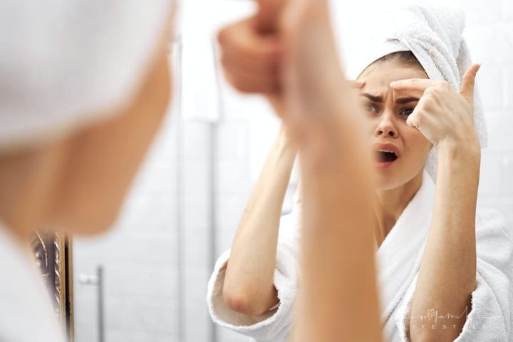 teen with head wrapped in towel noticing acne on forehead