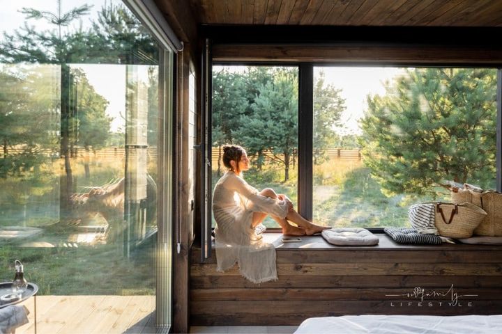Woman Enjoying Nature sitting in front of a large planeglass window at Country House