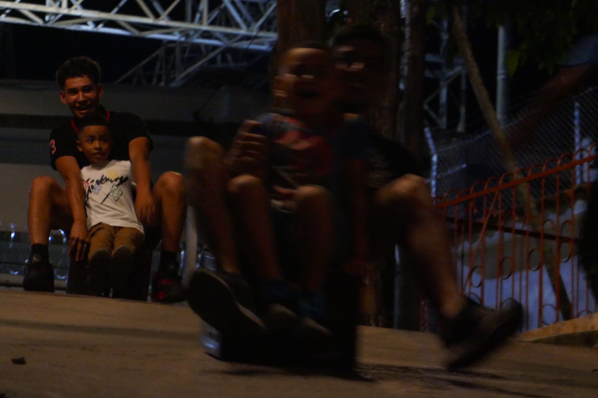 Des enfants et des adolescents glissent le long d'une route en béton sur des caisses en plastiques la nuit à Cali