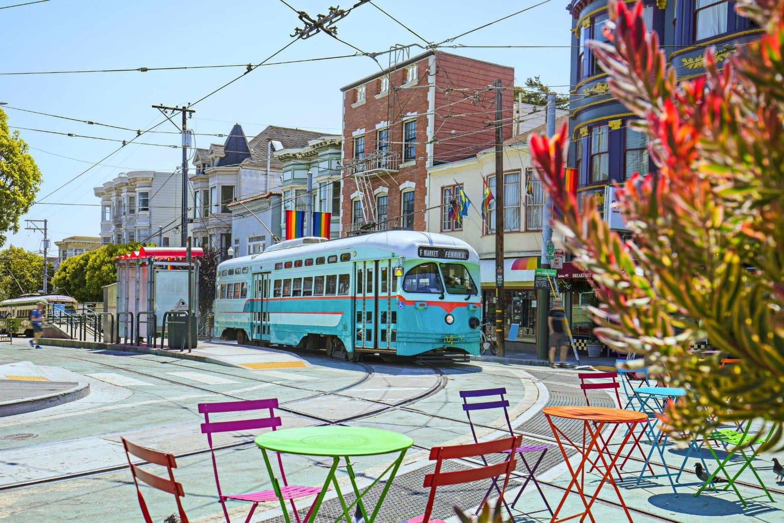 A teal F-line streetcar with bistro tables in the foreground