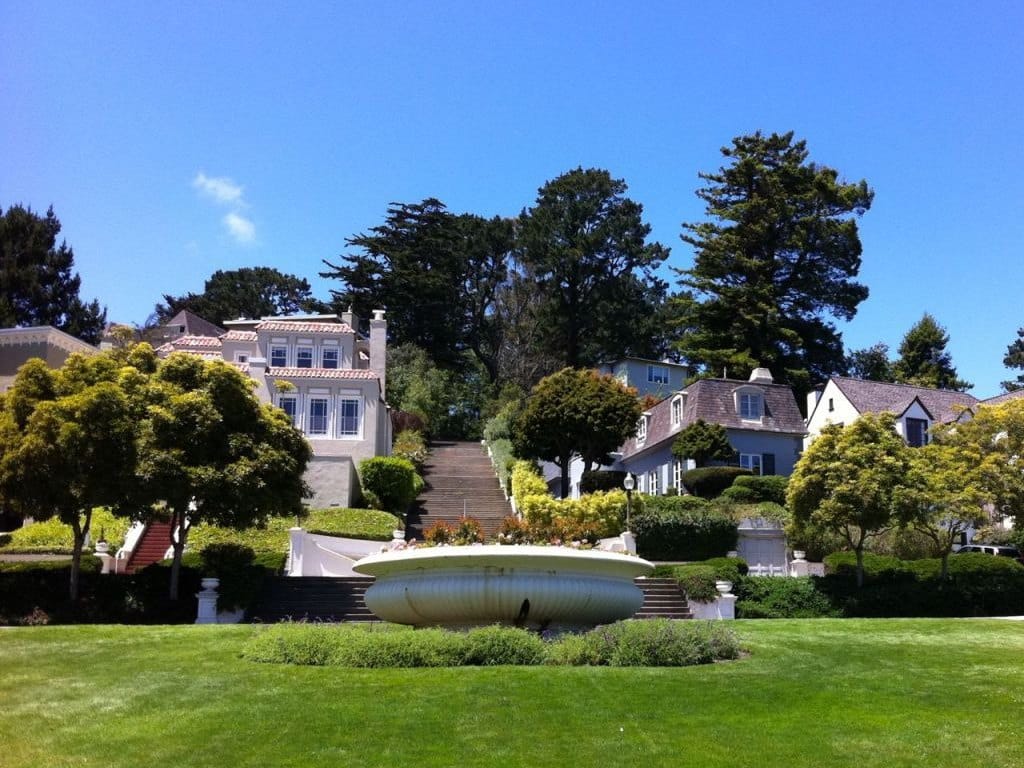 A grand stairway rising past a lawn and fountain toward Forest Hill homes
