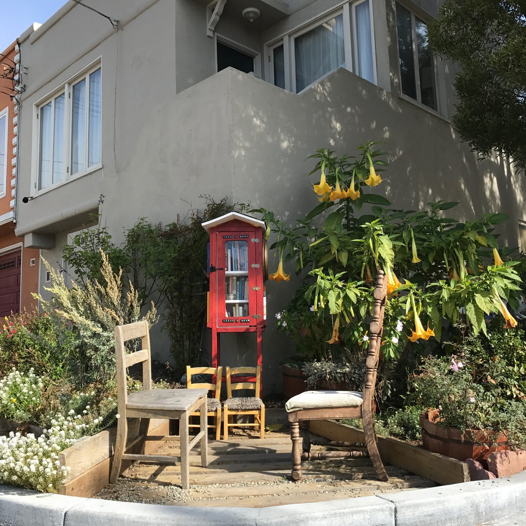A sidewalk garden with chairs and a little free library in Ingleside