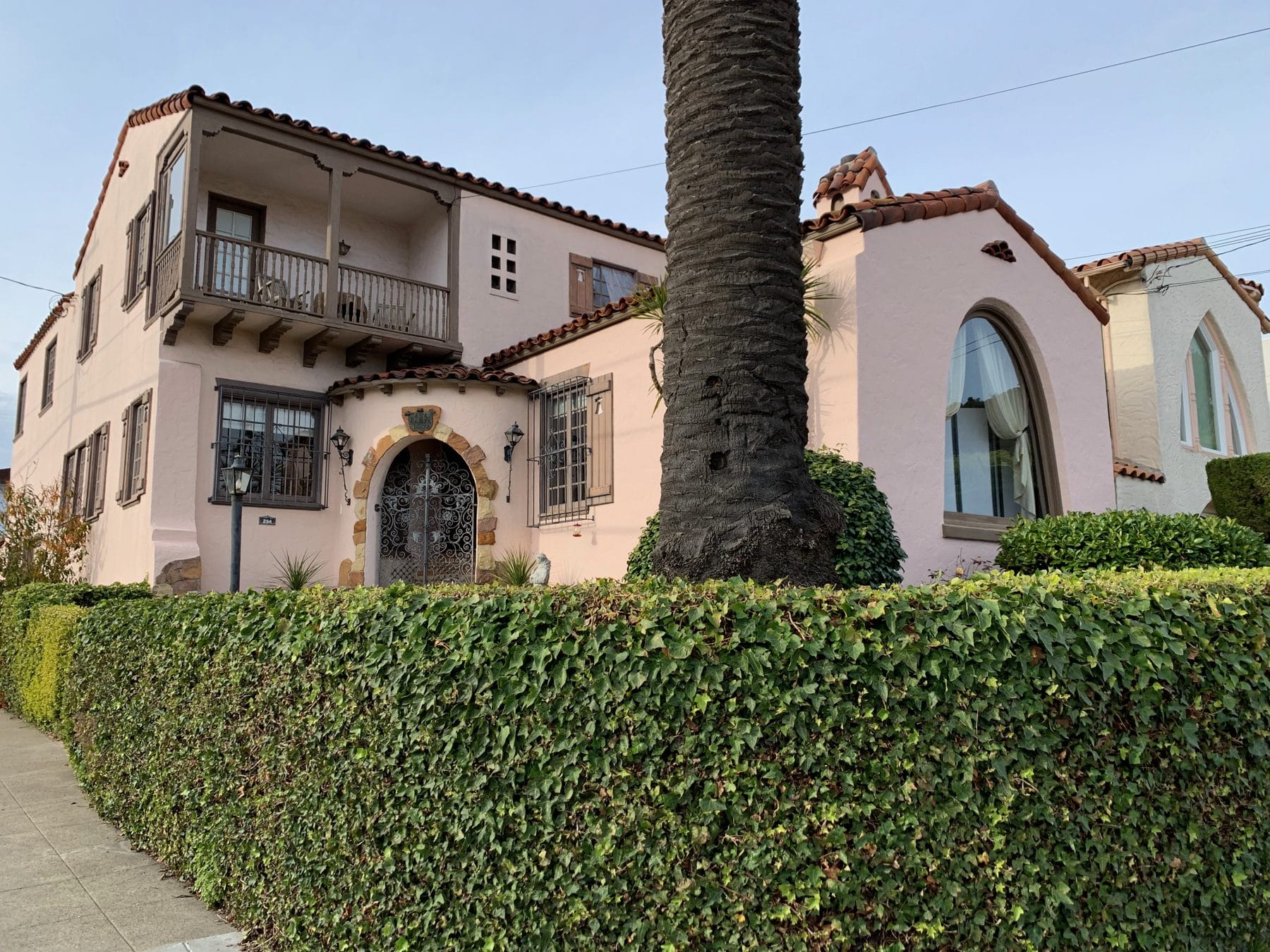 A pink Mediterranean house with a balcony behind a clipped hedge