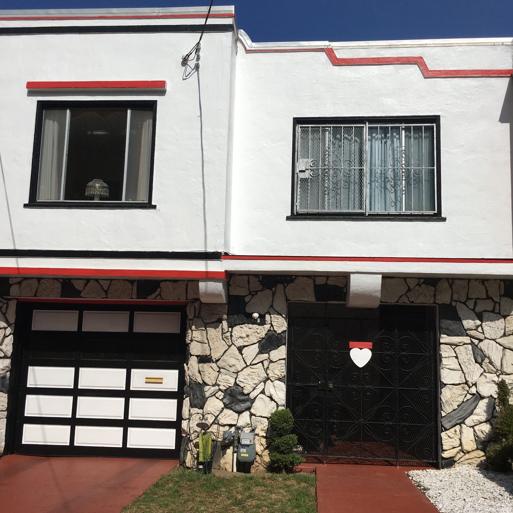 A white Streamline Moderne house with red trim and a stone base in Merced Heights