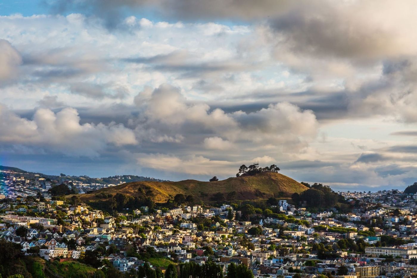 Bernal Hill rising above the houses of Bernal Heights under big clouds