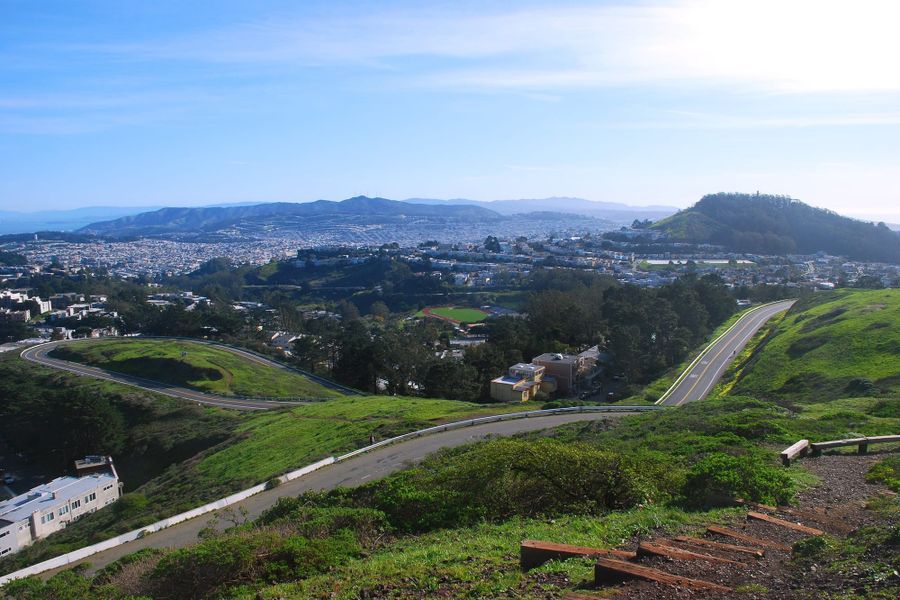 Twin Peaks Boulevard curving across the green summit, with the city beyond