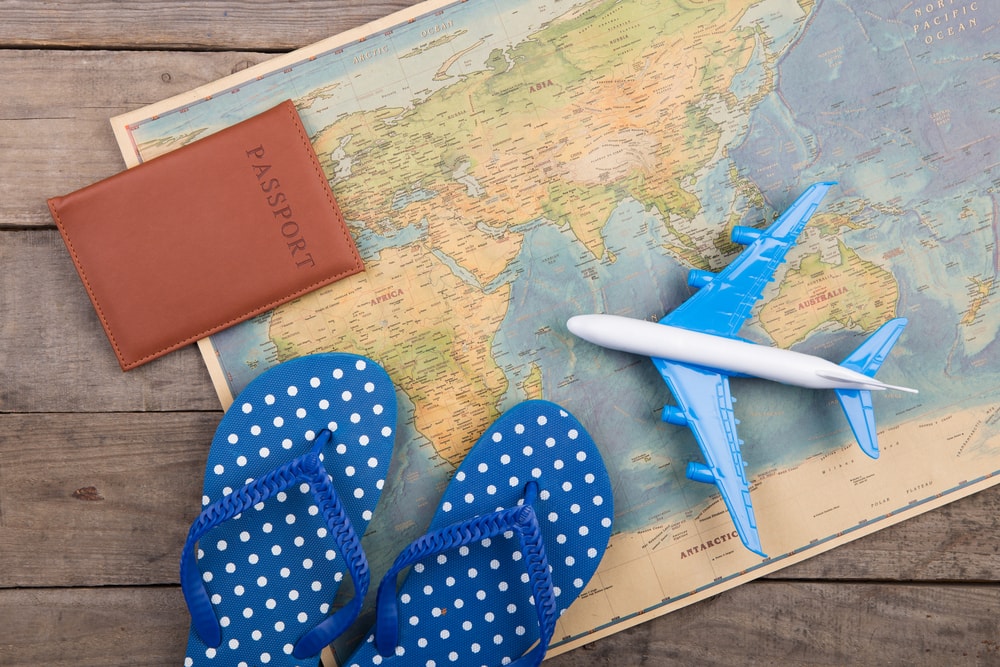 This is a photo of a a map with a passport, flip flops and a mini plane on it