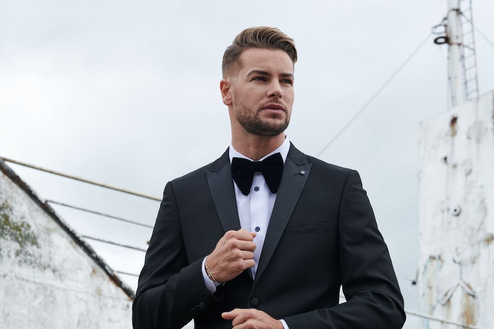 chris hughes wearing a suit and bow tie, looking into the distance