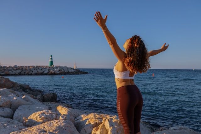 A woman practices yoga by the sea, her eyes closed. A lighthouse is in the distance.