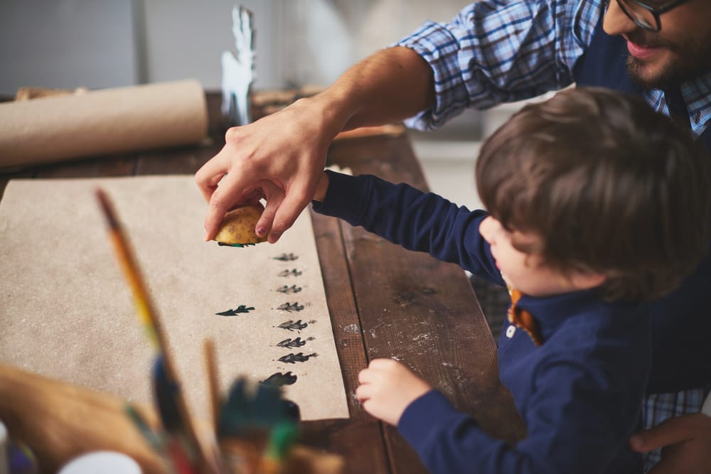 Young boy and father using a potato stamp on wrapping paper