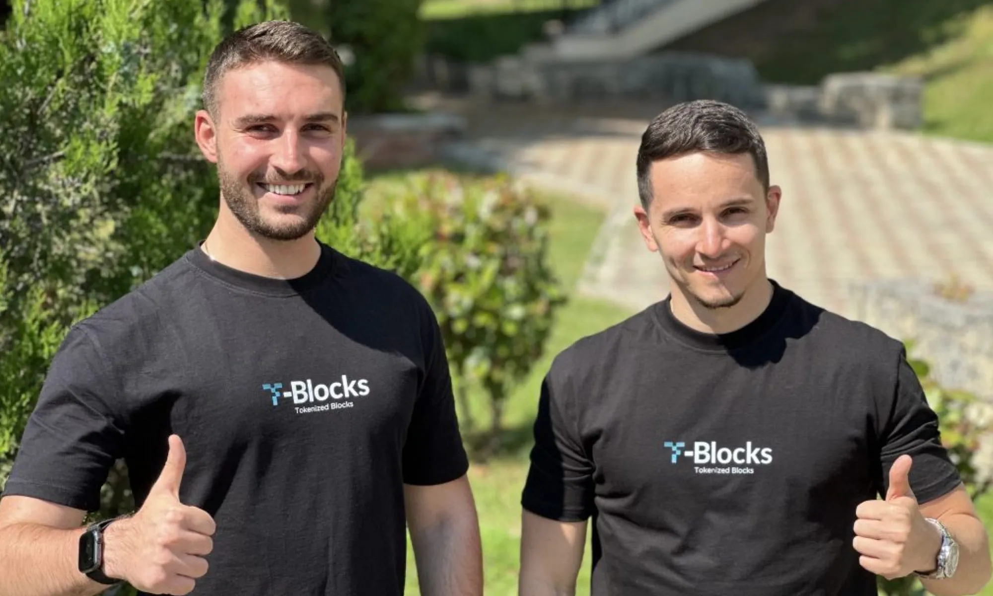 Two young men wearing black T-Blocks t-shirts smile outdoors, both giving thumbs up.