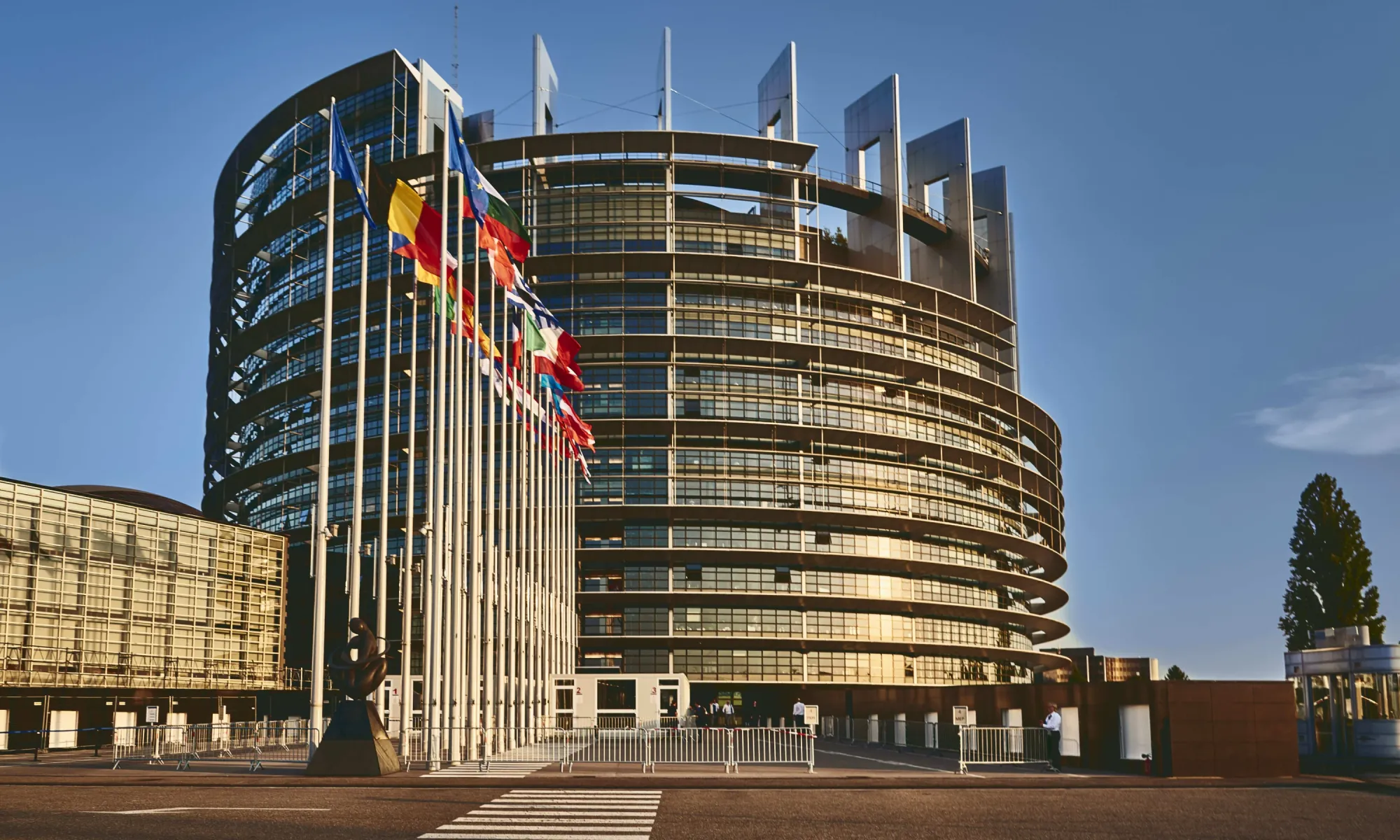 European Parliament building in Strasbourg, France, with European flags in front and a modern circular glass structure.