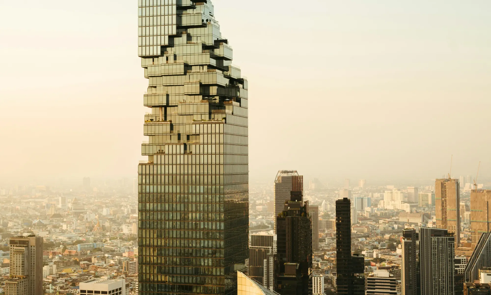 MahaNakhon skyscraper in Bangkok, Thailand, with its distinctive pixelated facade, towering over the city skyline during sunset.