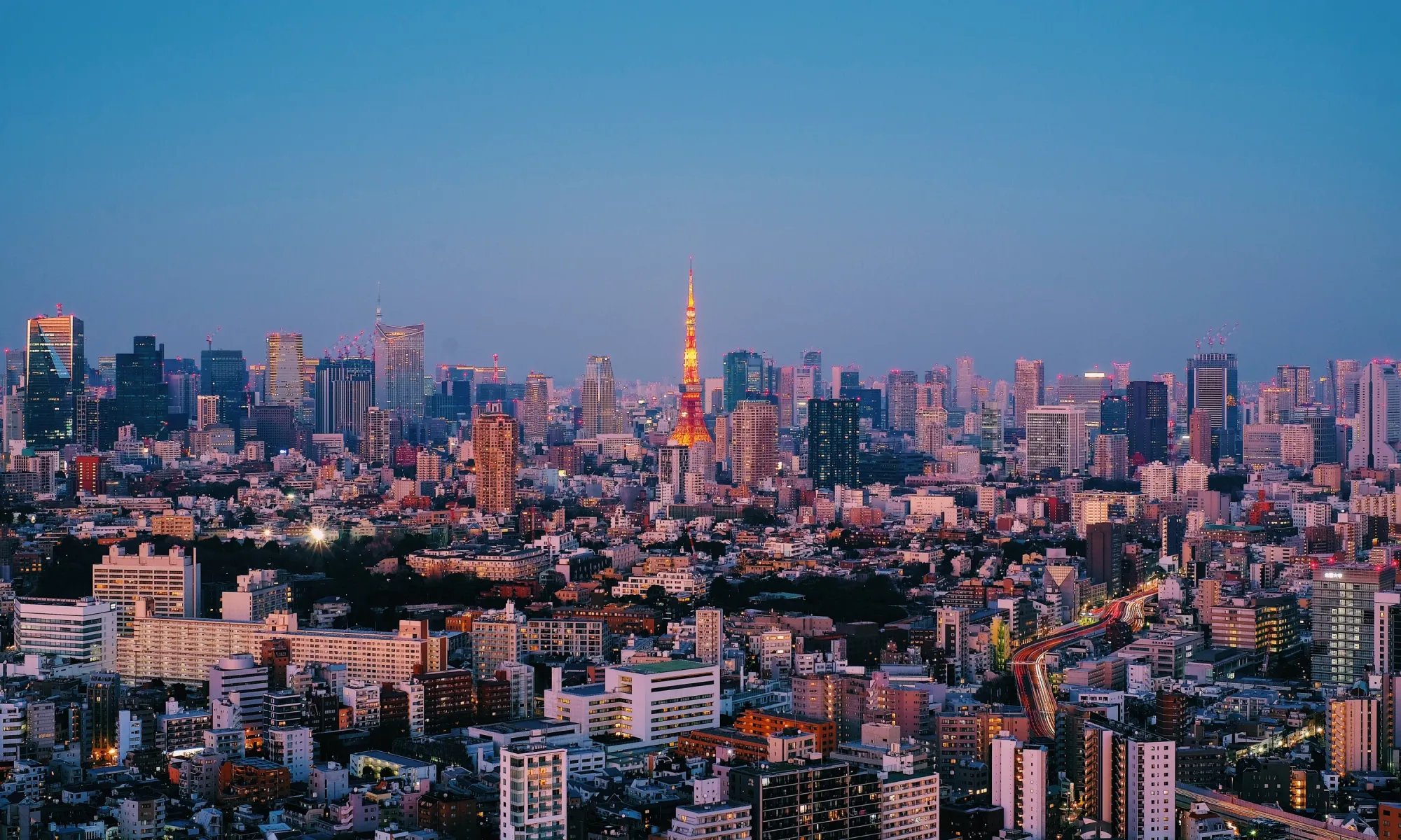 Panoramic skyline of Tokyo, Japan, with Tokyo Tower illuminated in the center at twilight.