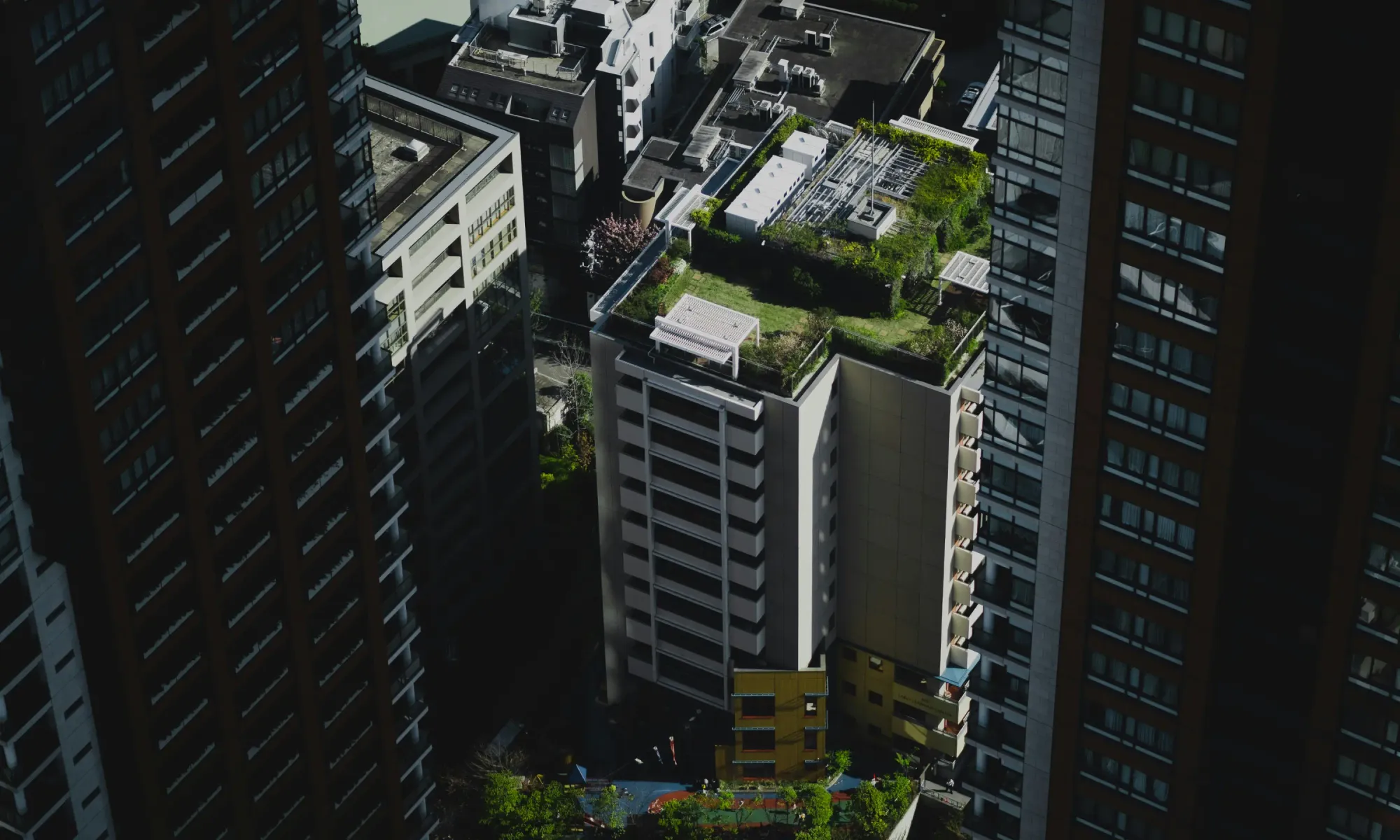 Aerial view of mid-rise and high-rise buildings in Japan, including a residential building with a rooftop garden surrounded by taller towers.