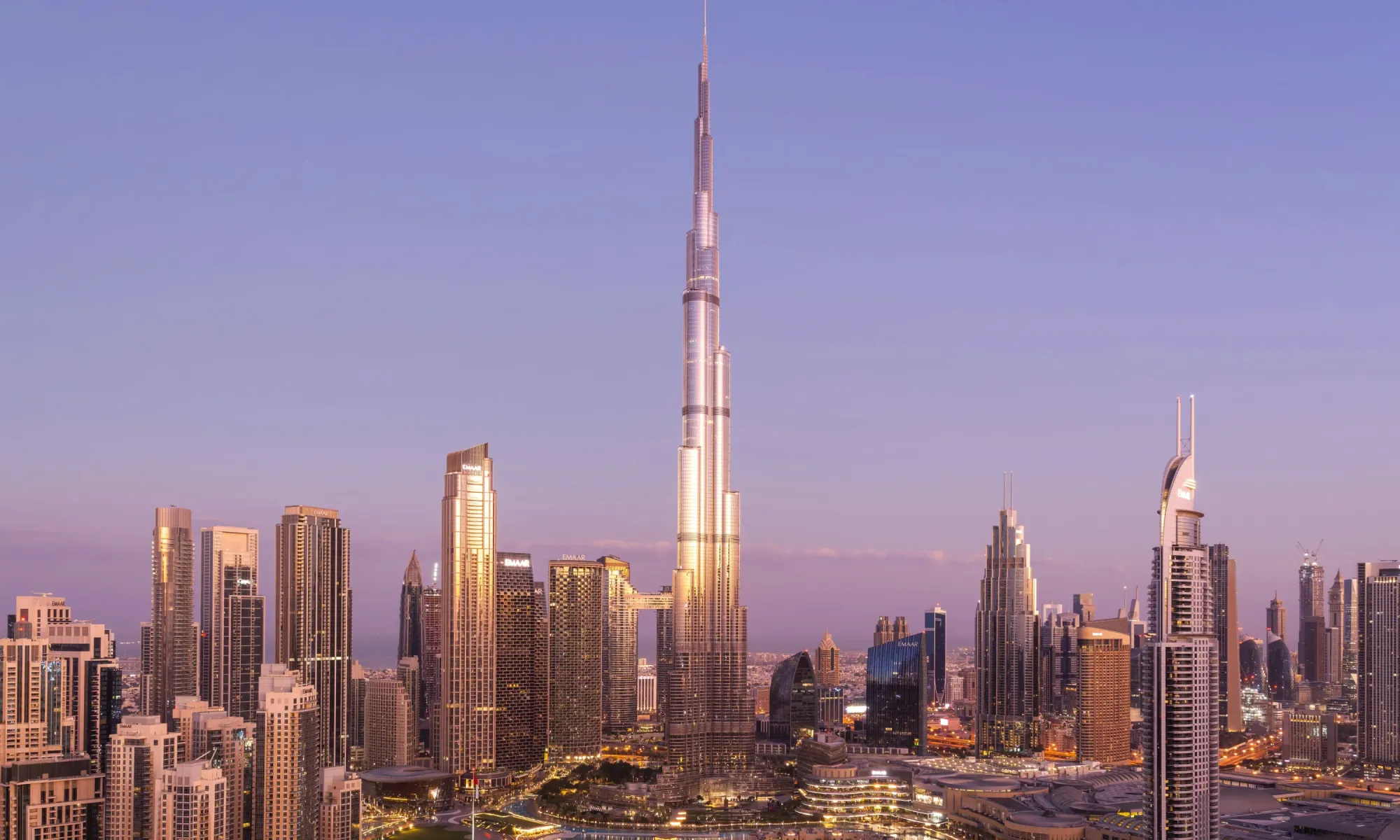 Aerial view of downtown Dubai at dusk, with the Burj Khalifa in the center surrounded by illuminated skyscrapers.