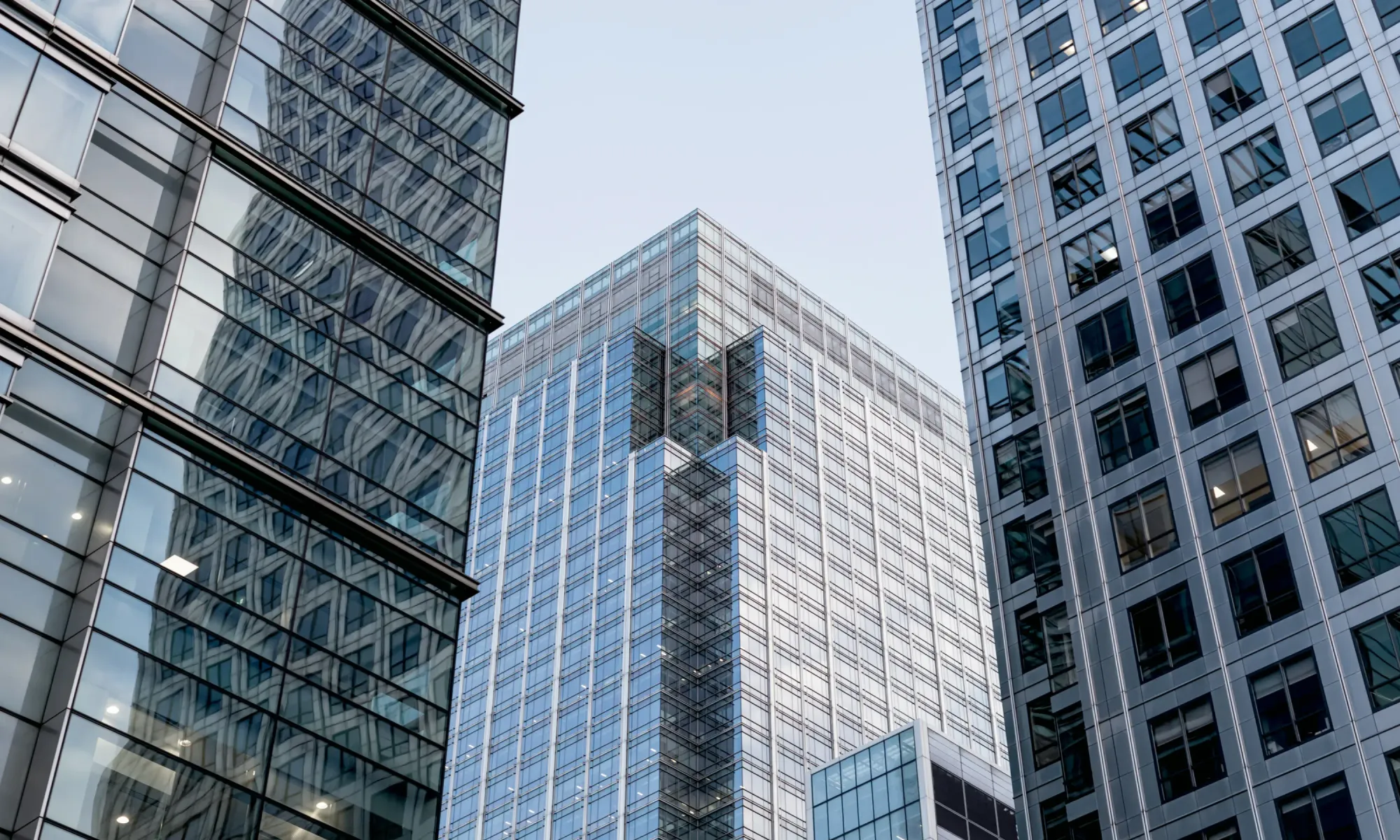 Tall glass skyscraper framed by other high-rise office towers, reflecting light in a financial district.