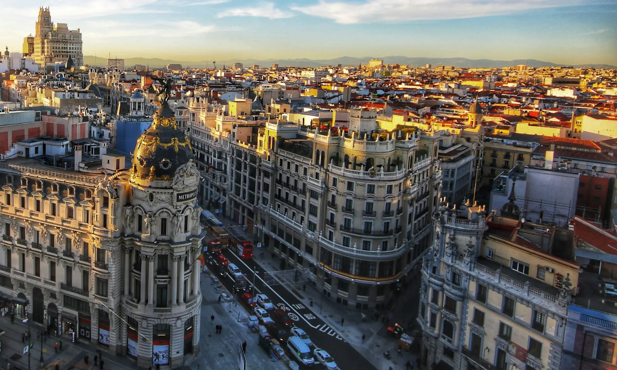 Aerial view of Madrid’s Gran Vía at sunset, featuring the ornate Metropolis Building with its domed roof and golden details.