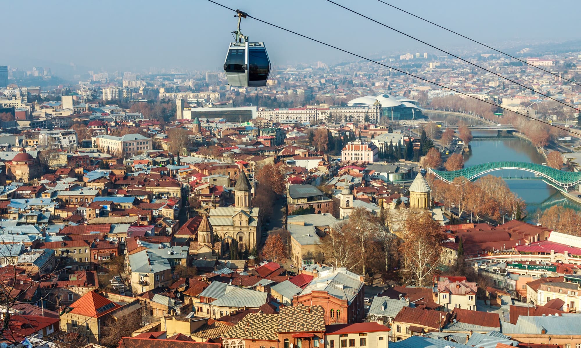 Tbilisi cityscape with cable car – A panoramic view of Tbilisi, Georgia, showing the old town, historic churches, and the modern Bridge of Peace, with a cable car passing overhead.