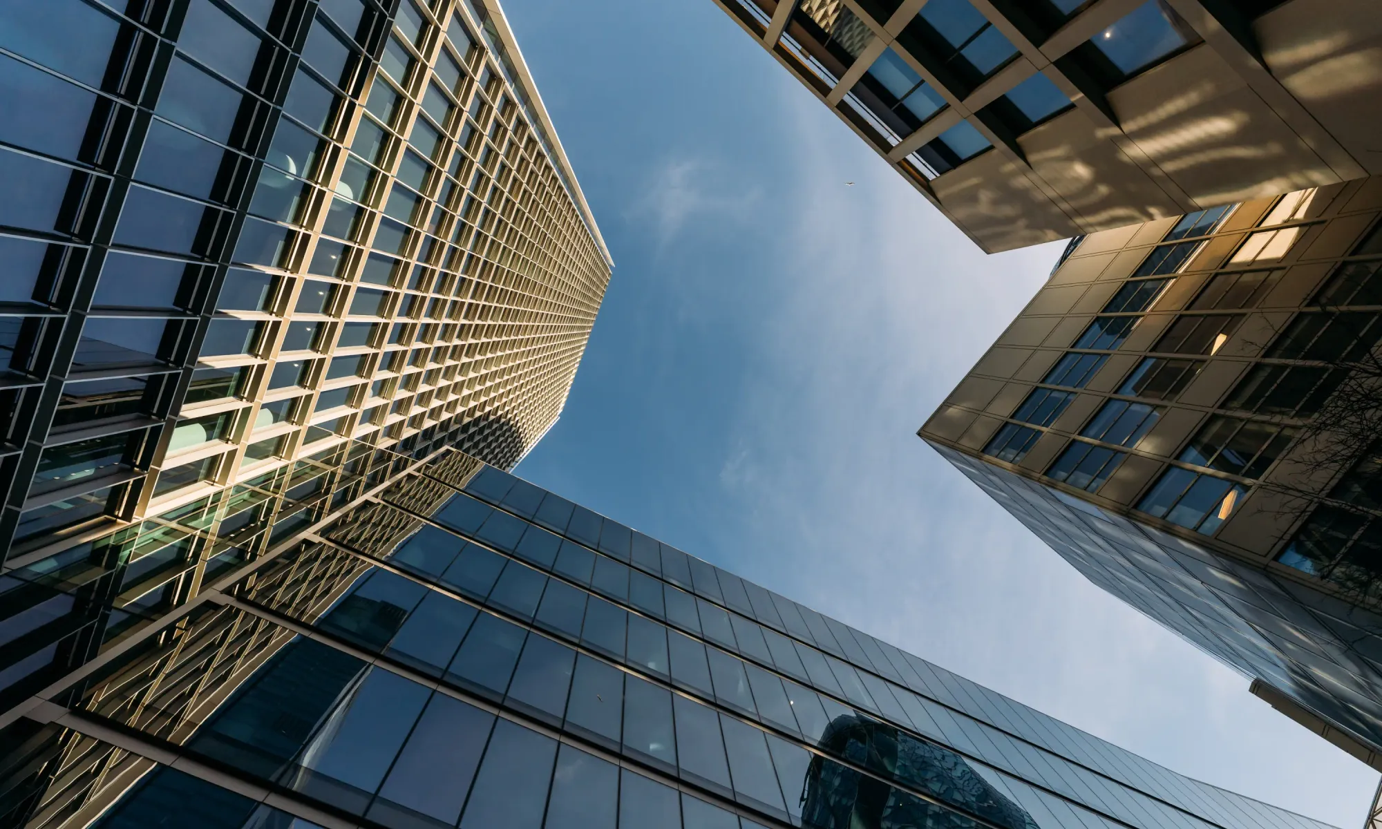 Looking up at tall office towers with glass and steel structures against a blue sky.