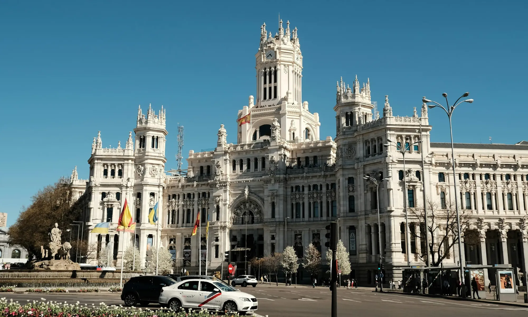 The Palacio de Cibeles in Madrid, a grand white neo-classical building with towers, flags, and a fountain in the foreground.