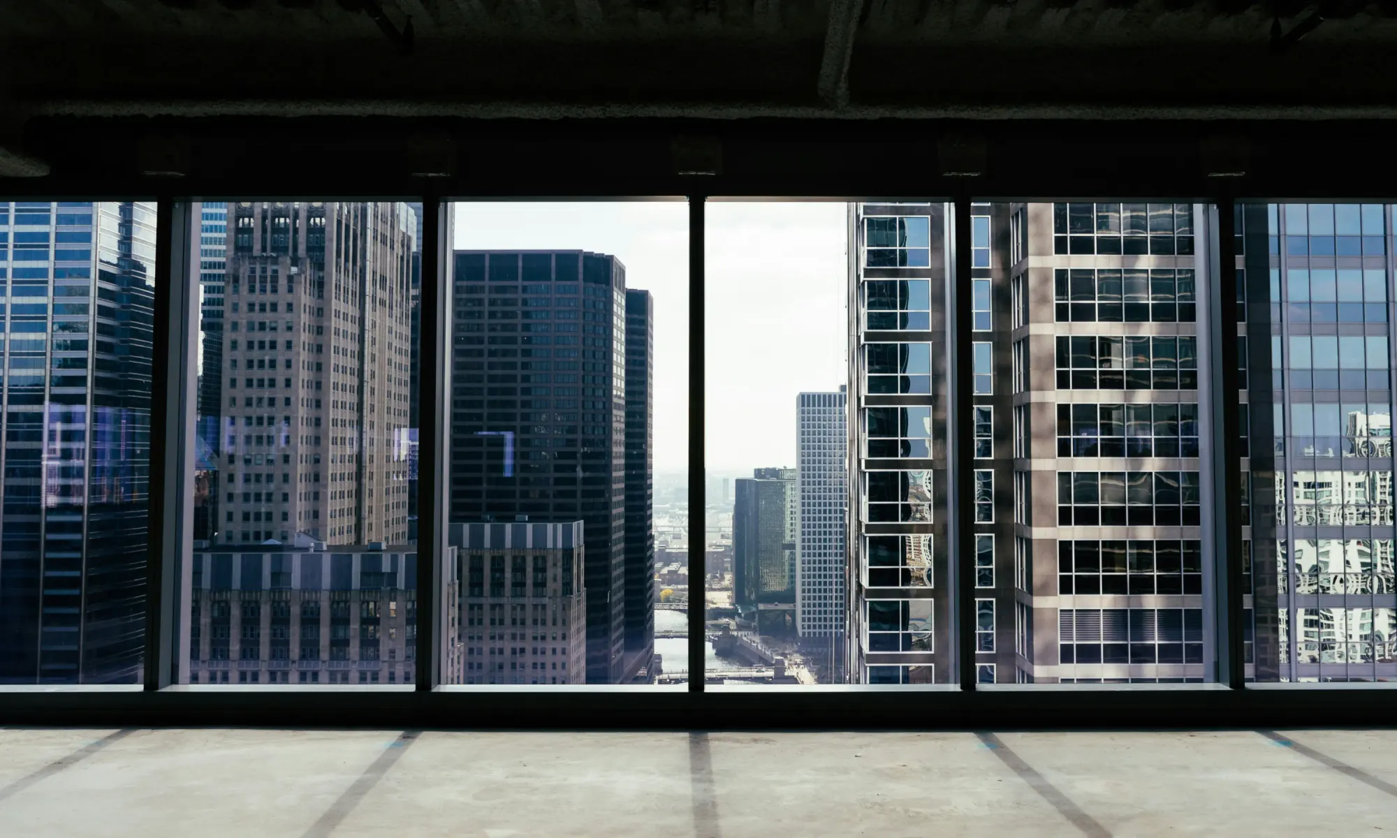 View of multiple skyscrapers through large office windows from inside an empty floor.
