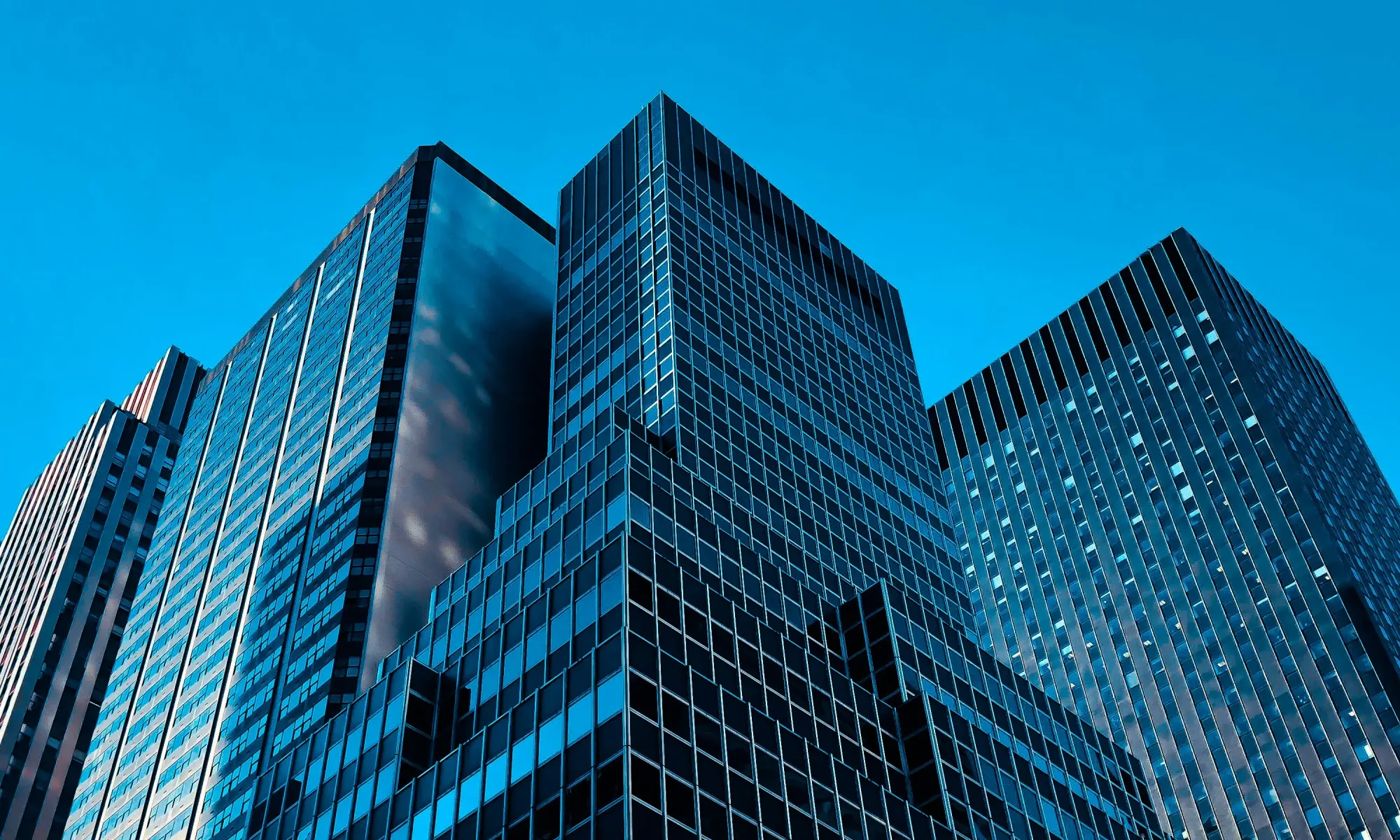 Cluster of tall glass skyscrapers reflecting blue light in a dense urban cityscape.