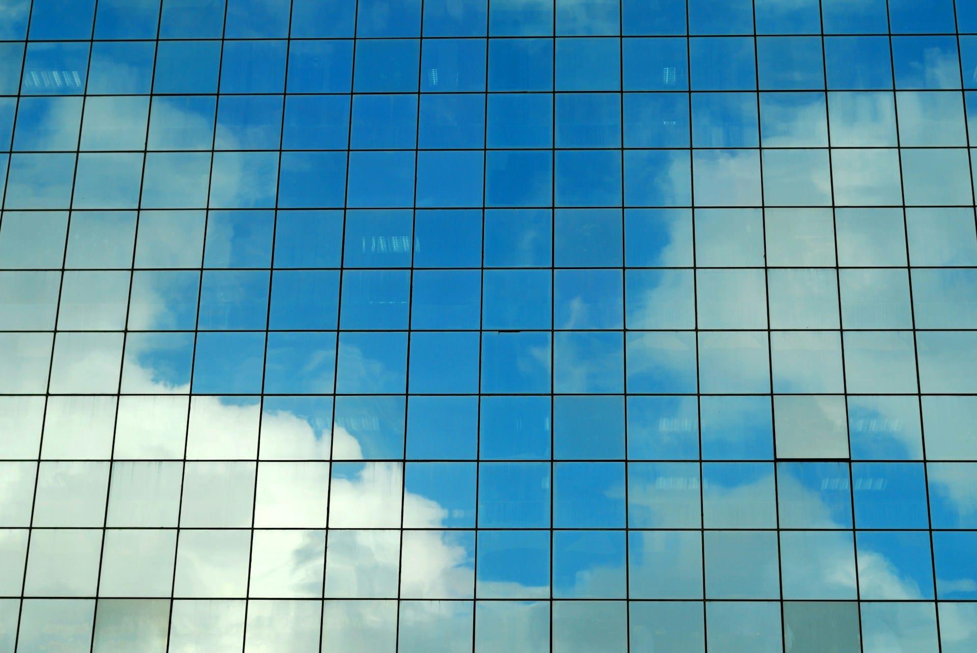 Modern glass office building reflecting sky — real estate technology