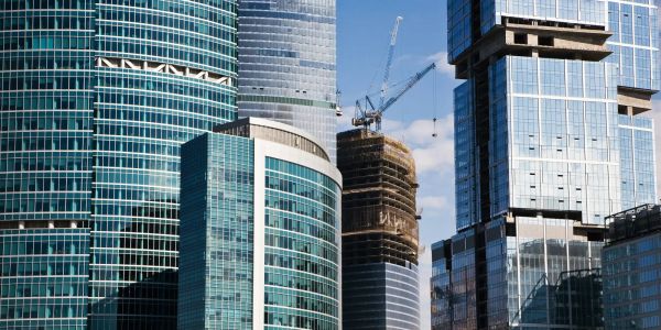 Cluster of modern glass skyscrapers with cranes and construction in progress, reflecting blue sky and clouds.