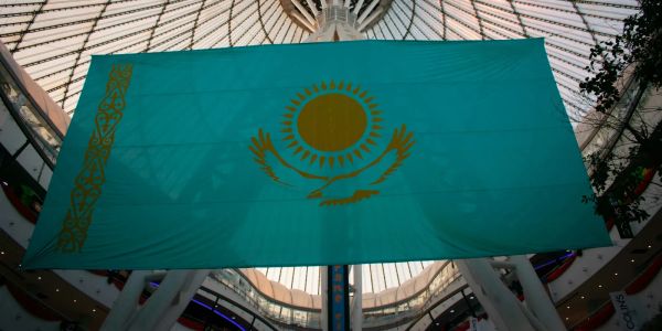 Large Kazakhstan national flag displayed indoors under a glass dome.