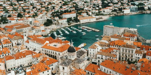 Aerial view of Dubrovnik’s old harbor with yachts, medieval walls, and historic stone buildings with red-tiled roofs.