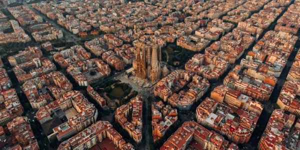 Aerial view of Barcelona at sunset with the illuminated Sagrada Família basilica towering over the city’s dense urban grid.