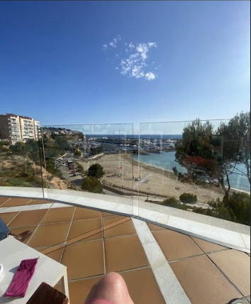 A person's legs on a tile floor overlooking a body of water

Description automatically generated