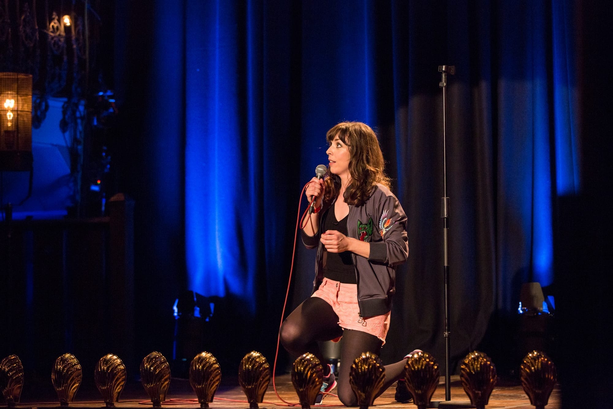 A woman kneels on stage holding a microphone
